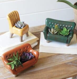 A yellow ceramic chair, green ceramic couch, and orange ceramic couch with tiny green succulent plants on top.